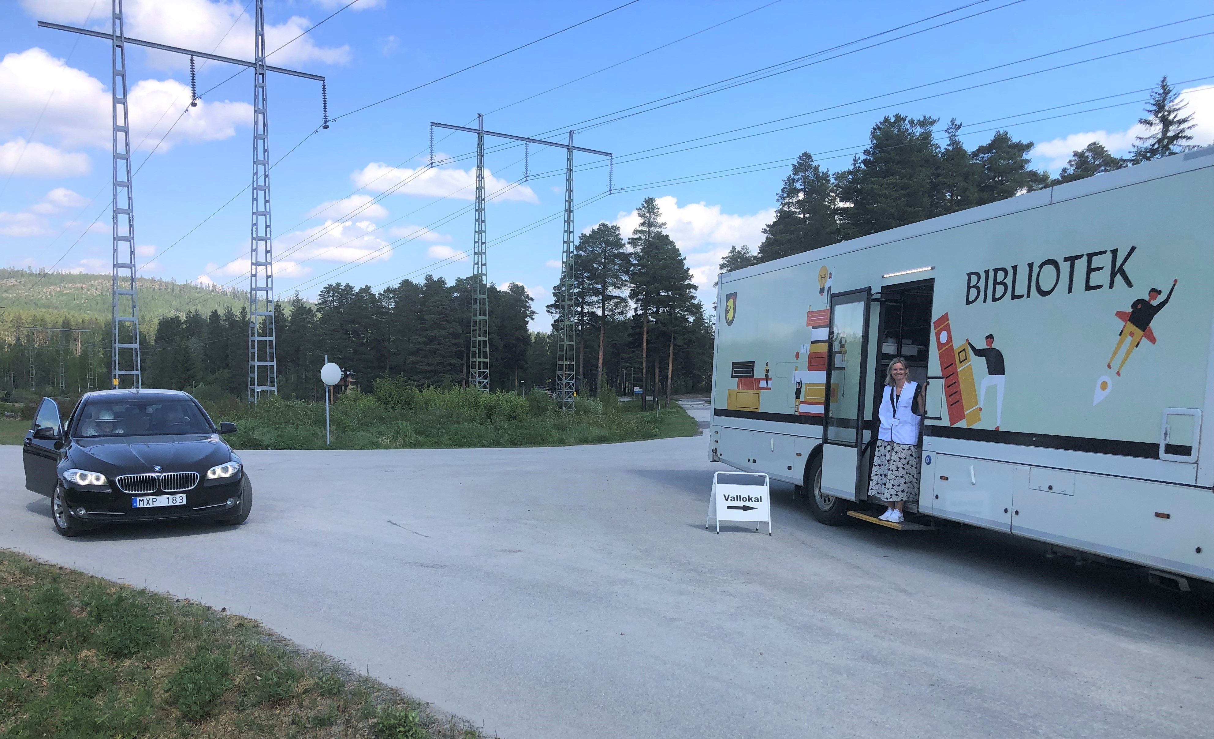 Bokbussen med en röstmottagare i dörröppningen och en bil som stannat utanför